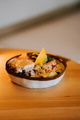 Healthy bowl featuring salmon, red rice, avocado, cucumbers, tomatoes, lettuce, and poached egg with Caesar sauce