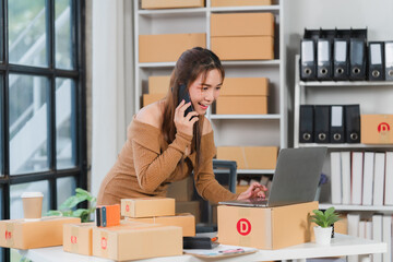 Online Business Woman:  A smiling young woman manages her thriving online business, efficiently handling a phone call while checking orders on her laptop, surrounded by neatly stacked packages.  