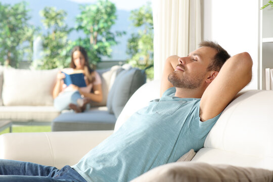 Man relaxing at home and his girlfriend reading a book in terrace