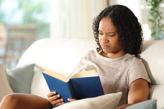 Disgusted black woman reading a paper book on a sofa