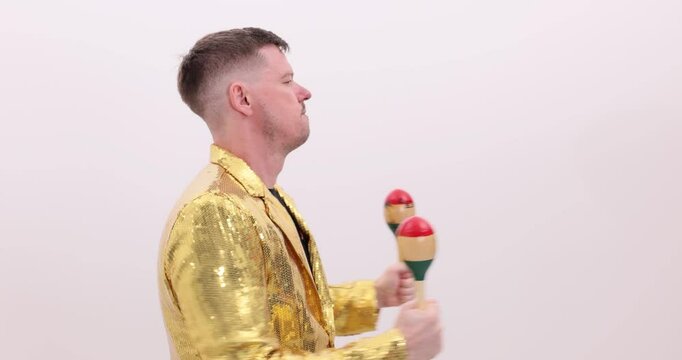 Energetic musician in golden jacket plays maracas on white background. Vibrant rhythmic musical performance at Latin culture dance party slow motion