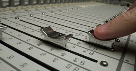 A man controls a mixing console while recording audio in the studio. Close-up of his hand, an...