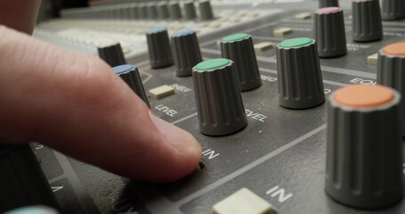 A man controls a mixing console while recording audio in the studio. Close-up of his hand, an...