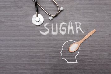 Stethoscope and Sugar is poured into human head silhouette with a wooden spoon on grey background...