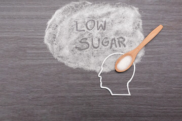 Wooden spoon pouring sugar into human head cutout on grey background, Low sugar diet and health...