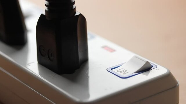 Finger presses the switch button to turn on of extension socket. Text "on" at the power switch button