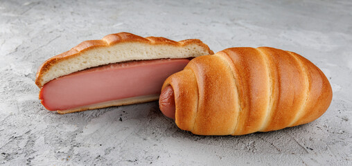 A cut and whole sausage in dough lie on concrete.