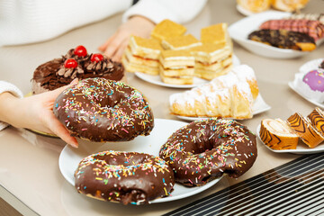 Woman's hand taking chocolate glazed donut from table with sweet food