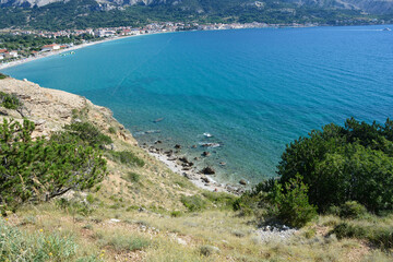 A view of Baska beach (Vela plaza) and the village of the same name, situated by the blue sea, as seen from the rocky western shore of Baska Bay in Croatia