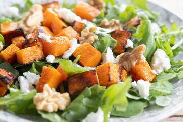 Pumpkin salad with arugula, walnuts and feta cheese on wooden. Close up