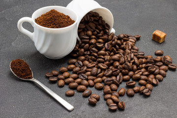 Ground coffee in cup and spoon. Roasted coffee beans are scattered from cup onto table