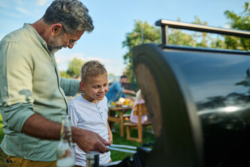 Grandfather teaching grandson grilling on barbecue for family reunion