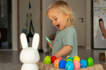Obraz premium Child joyfully decorating colorful Easter eggs in a bright spring setting at home