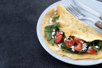 Stuffed omelette with tomatoes and spinach on black slate background. Copy space