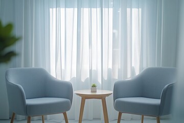 Two light blue armchairs face each other across a small wooden table in front of a sheer window curtain.
