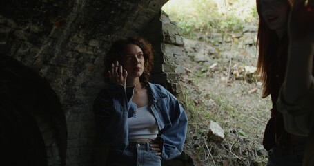 Three friends are smiling and talking standing near a ruined historical building. They smoke. A...