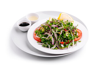 Fresh mixed salad served on a white plate with dressing choices and lemon wedge
