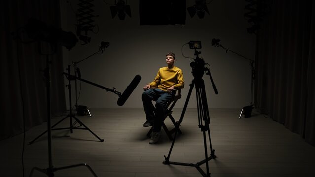 Studio for photo video production with lighting equipment and cyclorama, model actor sits on director chair in the middle and recording interview.