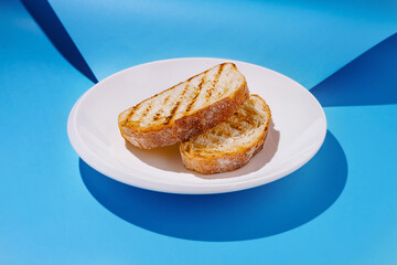 Sliced grilled bread on a white plate against a blue background creating a vibrant food display