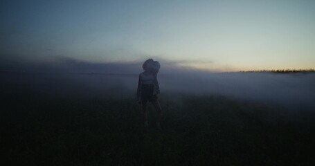 Obraz premium A young woman smiles at the camera while standing in a field amid thick smoke. Summer evening