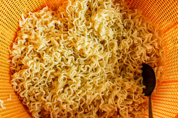 A close-up shot of cooked instant noodles in an orange plastic colander. The noodles are light...