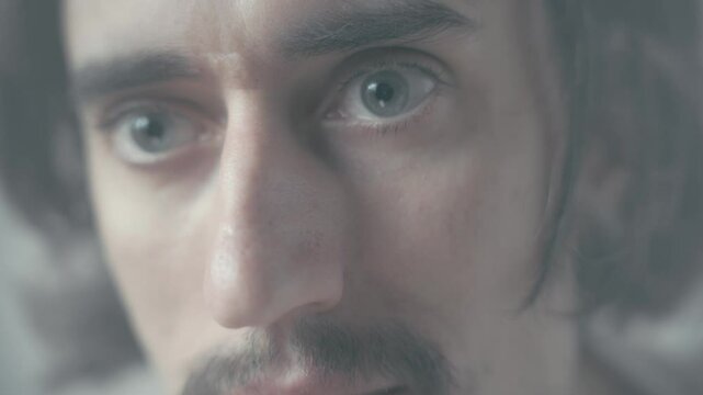 Confident Man Close-Up Focused man with long hair and a mustache gazes intently with big eyes in an atmospheric setting