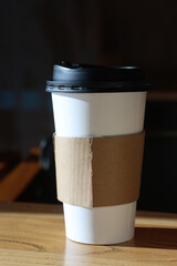 Disposable coffee cup with lid on wooden table in coffee shop mock up