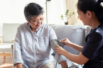 Young Asian woman nurse take care senior woman at nursing home, checking blood pressure for observe...
