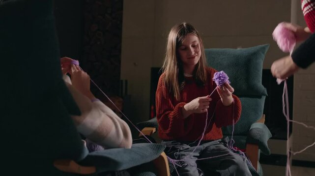 A young girl in an orange sweater untangles purple yarn with the help of others in a cozy room during a family crafting session.