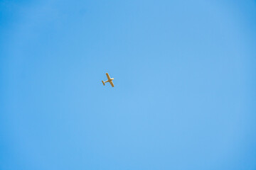 Minimalistic view of a small airplane flying against a bright blue sky, emphasizing open space
