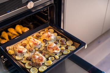 A baking tray with French-style pork, potatoes, mushrooms, and cheese, alongside baked chicken 