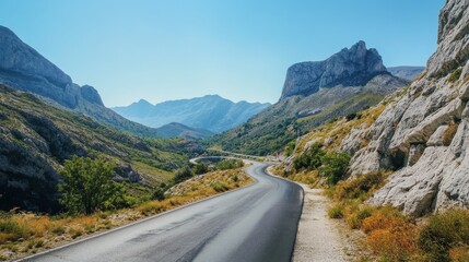 Fototapeta premium 75.A winding asphalt road cutting through a mountainous region, with rocky hills and steep cliffs on either side. The road is smooth and well-maintained, stretching ahead in a series of curves that
