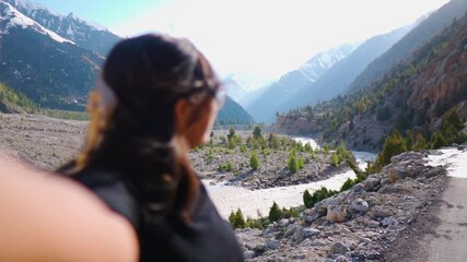 Rack focus shot of Girl looking at mountain landscape in Miyar Valley, Lahaul, India. Tourist taking selfie video, making travel vlog for her social media channel.