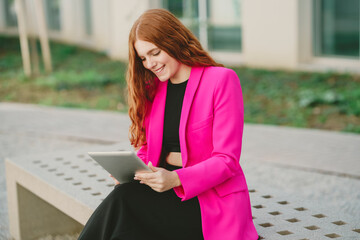 A stylish woman is happily using her tablet outdoors, enjoying fresh air and nature