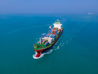 the aerial perspective of a cargo ship being loaded and unloaded at a bustling seaport and sailing out of the mainland