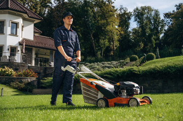 Cutting the grass by lawn mover. Professional gardener is on the lawn