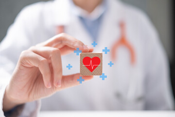 Professional healthcare medical worker holding red heart with cardiogram on wooden block...