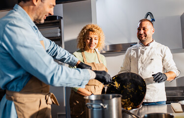 Couple enjoying a cooking class with a chef preparing meal in the kitchen.