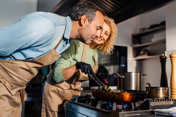 Couple enjoying a cooking class with a chef preparing meal in the kitchen.