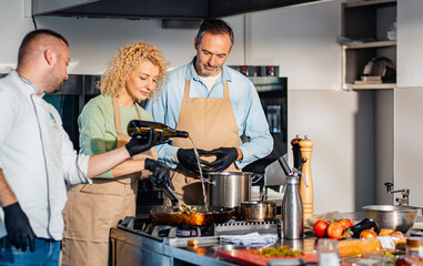 Couple enjoying a cooking class with a chef preparing meal in the kitchen.