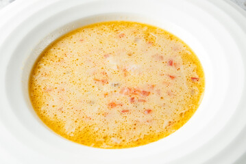 A creamy bowl of soup with a rich texture, featuring bits of tomato for added flavor. The light...