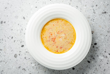 A creamy bowl of soup with a rich texture, featuring bits of tomato for added flavor. The light orange hue suggests a savory taste, perfect for a comforting meal.