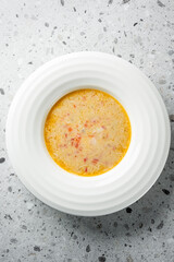 A creamy bowl of soup with a rich texture, featuring bits of tomato for added flavor. The light orange hue suggests a savory taste, perfect for a comforting meal.