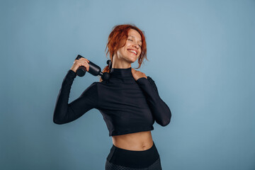 Black electric massager, in fitness clothes. Woman is in the studio against background