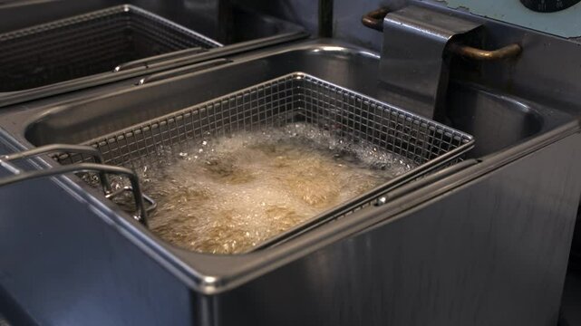 Tank of Country Style Potatoes Being Lowered Into Boiling Oil of Commercial Industrial Deep Fryer, Street food
