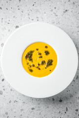 A vibrant plate featuring a smooth, creamy orange soup, artistically swirled with green herb oil. The dish combines culinary artistry with color contrast, perfect for gourmet presentations.
