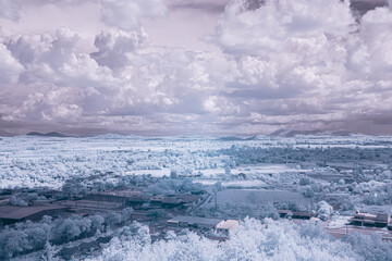 A landscape viewed in infrared light. A vast expanse of trees, fields, and clouds