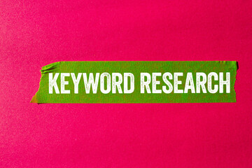 Keyword research message written on ripped torn green paper tape on pink background. Conceptual...