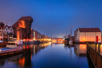 Obraz premium Beautiful architecture of the old town in Gdansk by the Motława river with a historic port crane at wintery night. Poland
