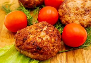 Fried chicken cutlets with vegetables on a wooden background. Meat balls with tomatoes and herbs on a wooden board.